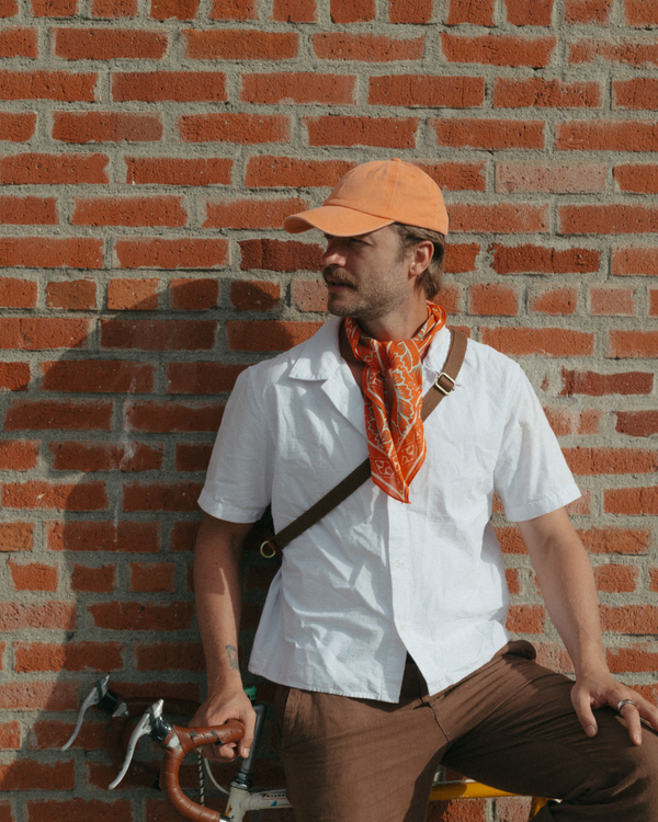 Model wearing a blank orange Classic Cap beside a brick wall