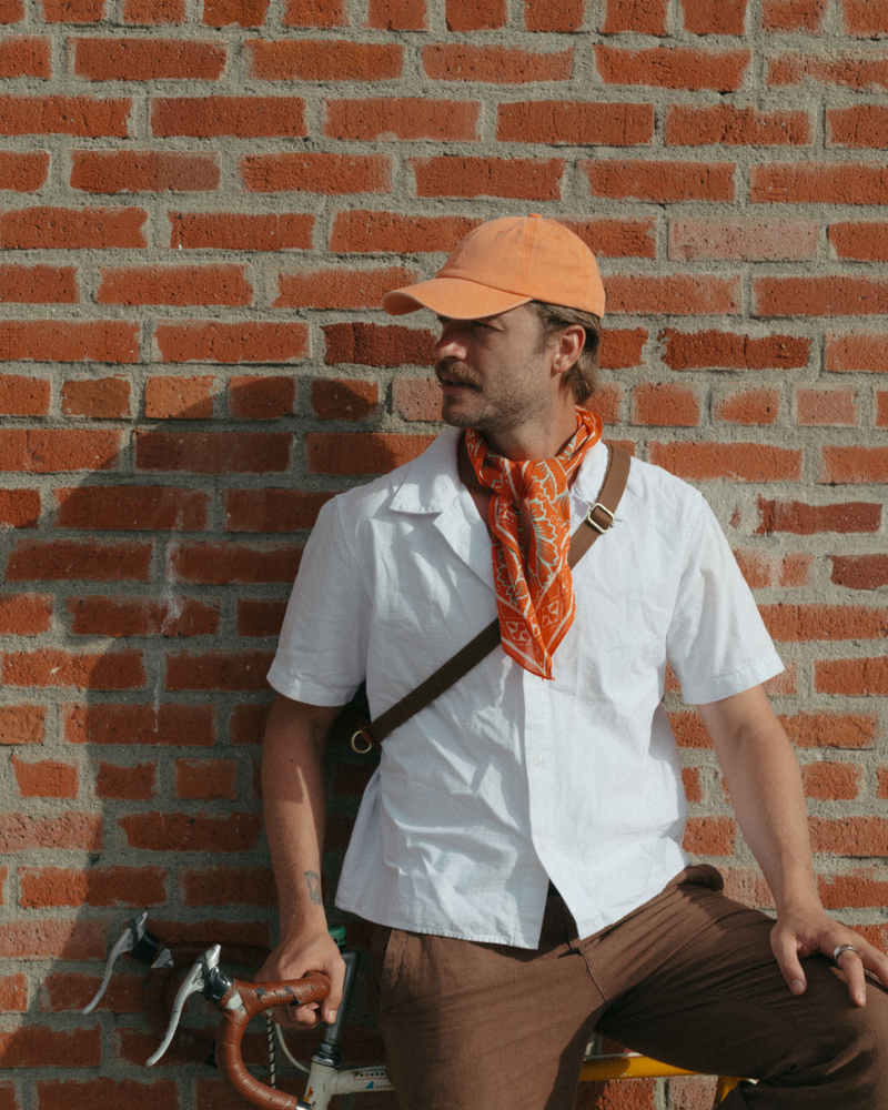 Model wearing a blank orange Classic Cap beside a brick wall