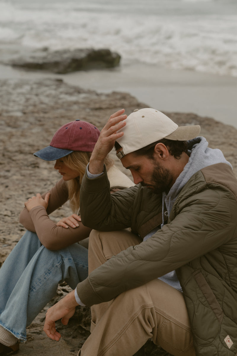 Two models wearing wine and navy and cream and khaki Classic Caps by the coast
